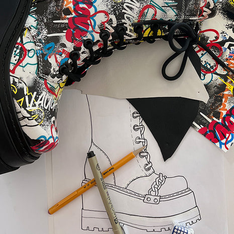 Image of a Sketch of a product with the actual product laying on top. The product is a double platform boot with a graffiti print.